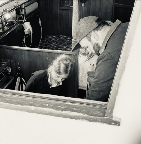 Black-and-white photo of Captain Mark below deck in the boat's cabin with two young crew members