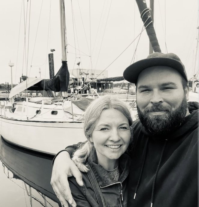 Black-and-white photo of Captain Mark and his wife Amy at the dock in front of a sailboat